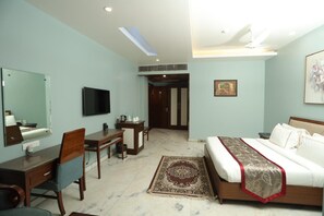 A hotel room with a bed, desk, chair, television, and a mirror. - Leela Grande Hotel (Karnal)