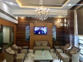 A modern living room with a television mounted on the wall, a chandelier, and a sofa with patterned cushions.
