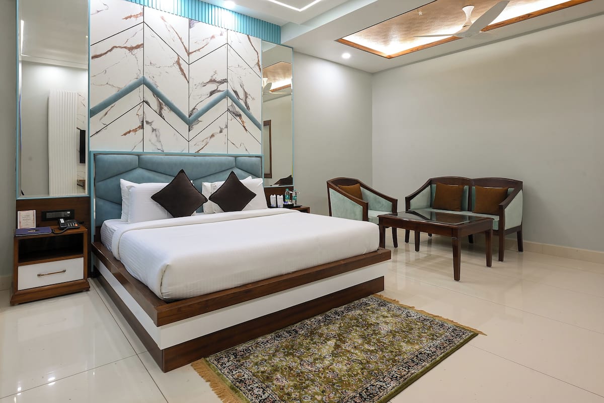 A modern hotel room with a large bed, a desk, two chairs, and a decorative wall.