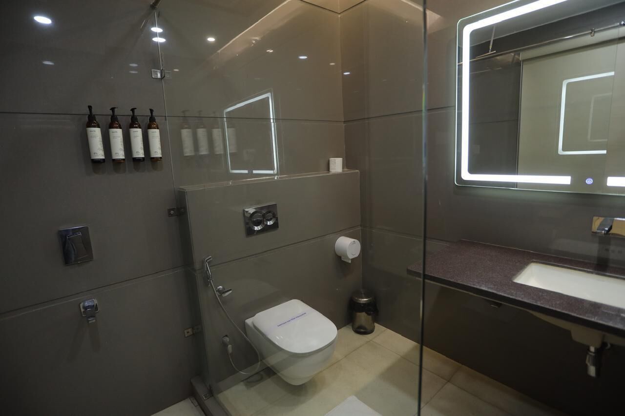 A modern bathroom with a glass shower enclosure, a toilet, a sink, and a mirror with LED lighting.