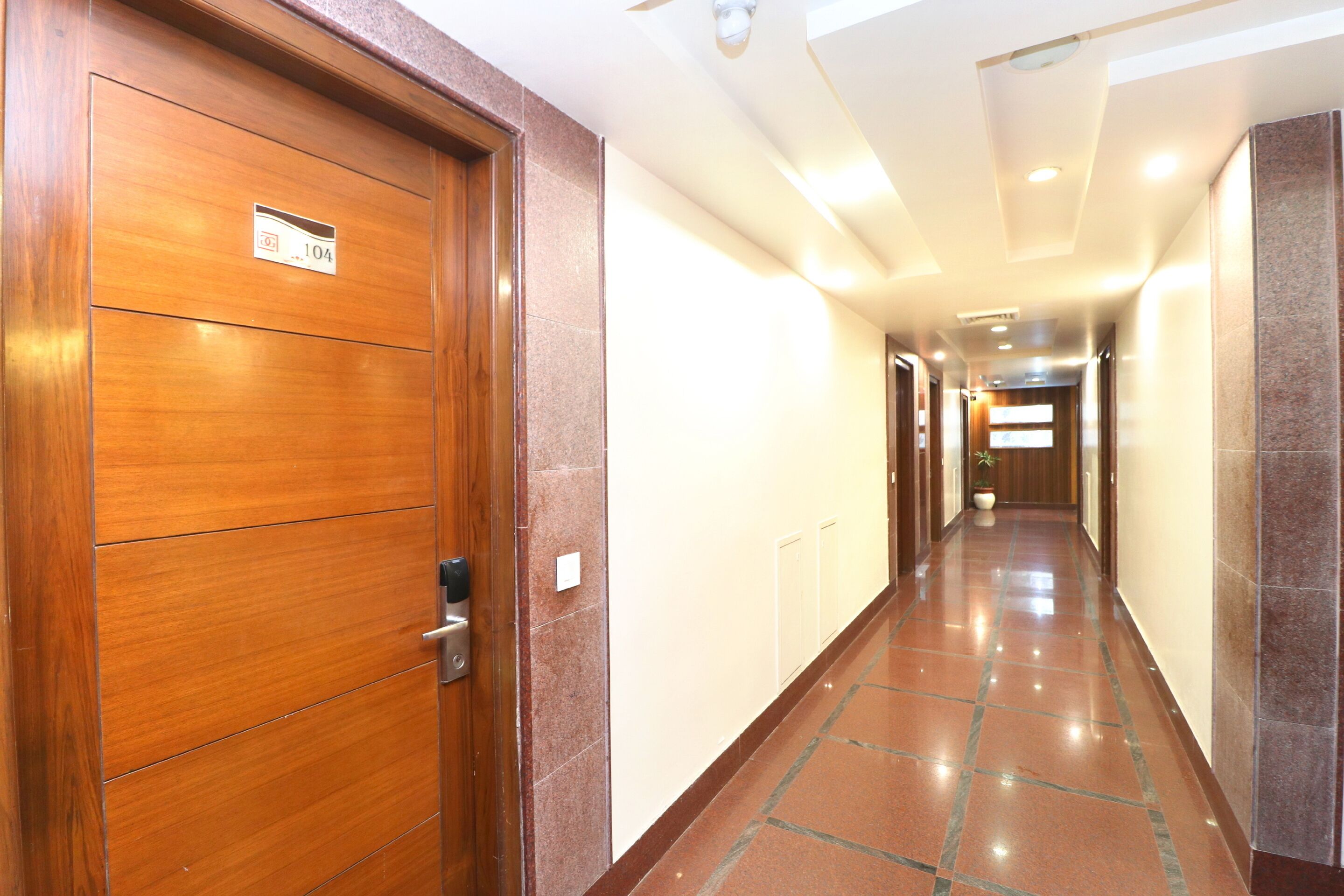 Un corridoio d'hotel con porte in legno, pavimento piastrellato e soffitto con illuminazione a incasso.