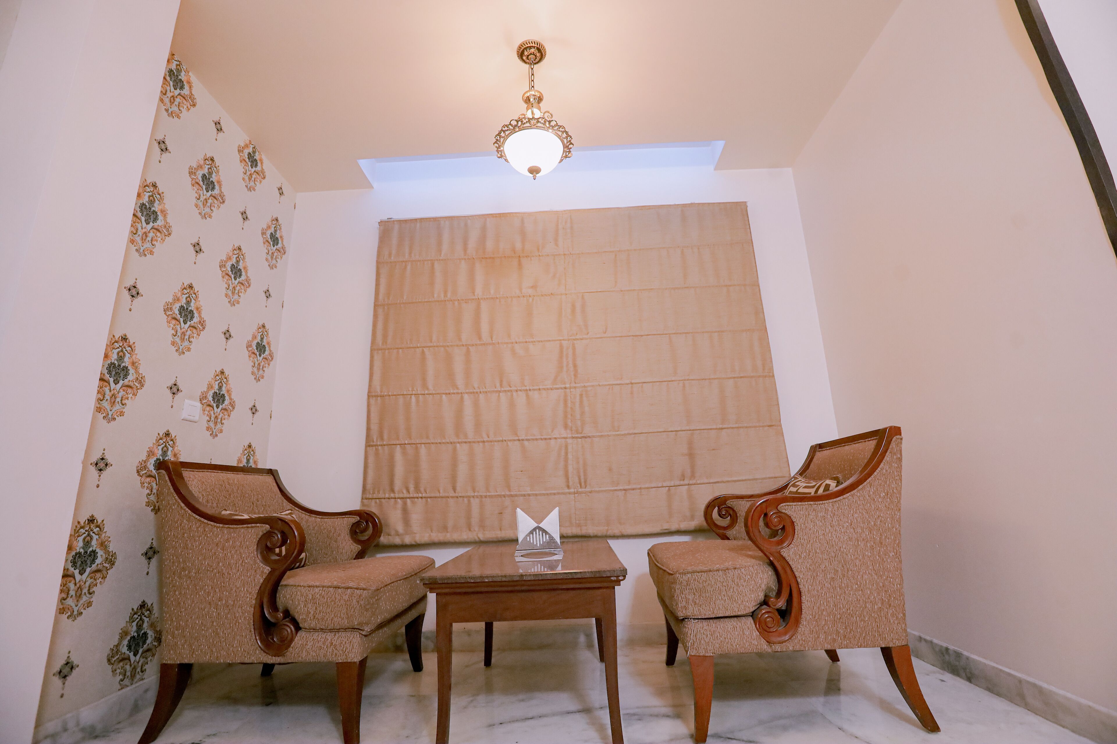 A room with two ornate chairs, a small table, and a large window with a blind.