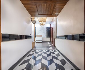 A hallway with a geometric patterned floor, a wooden ceiling, and a wall-mounted clock. - Leela Grande Hotel (Karnal)