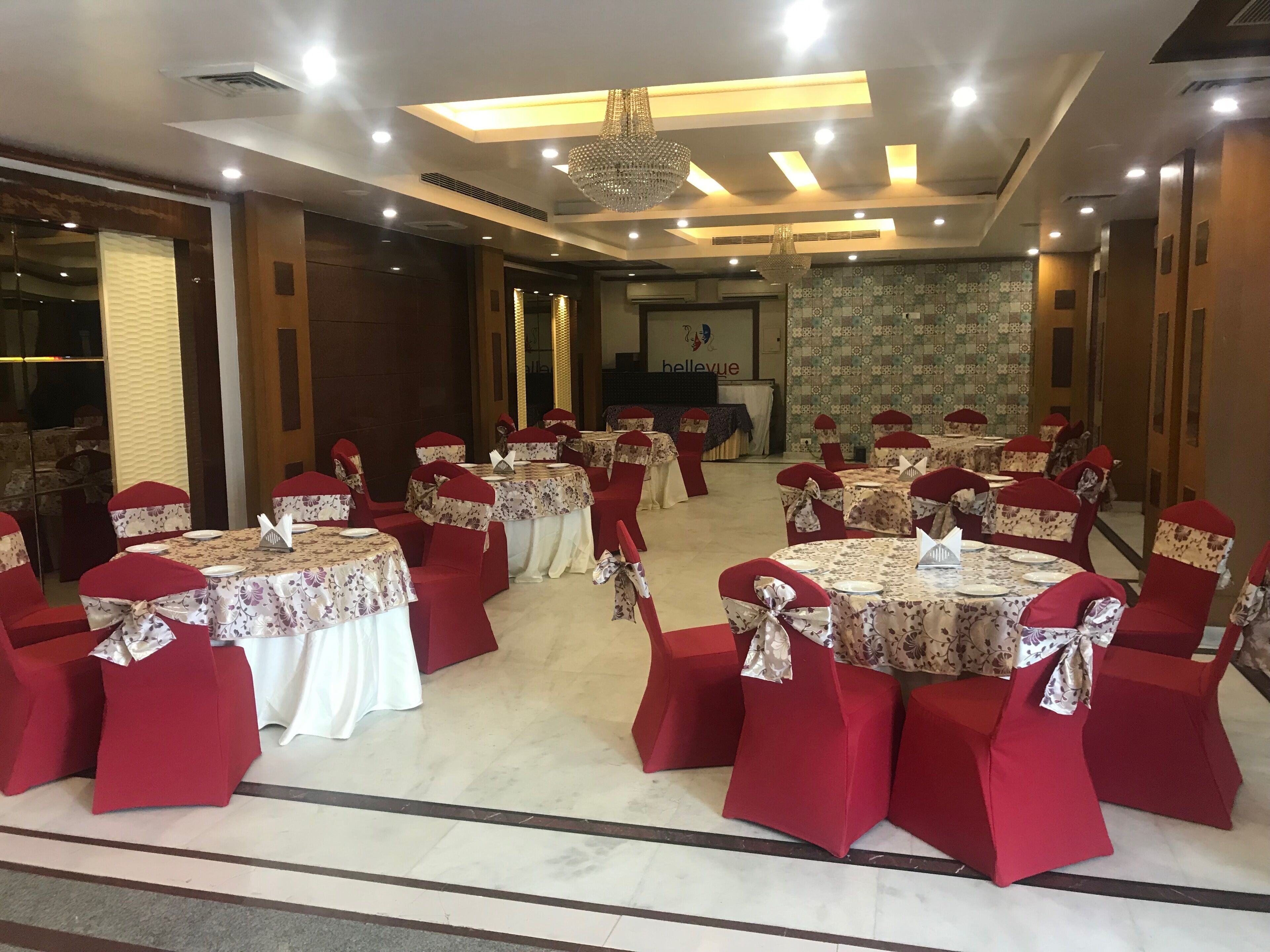 Un salón de banquetes con mesas redondas, sillas rojas y una araña de cristal.