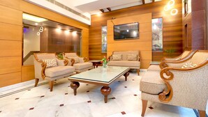 A modern lobby with a glass-top coffee table, wooden panel walls, and a large mirror. - Leela Grande Hotel (Karnal)