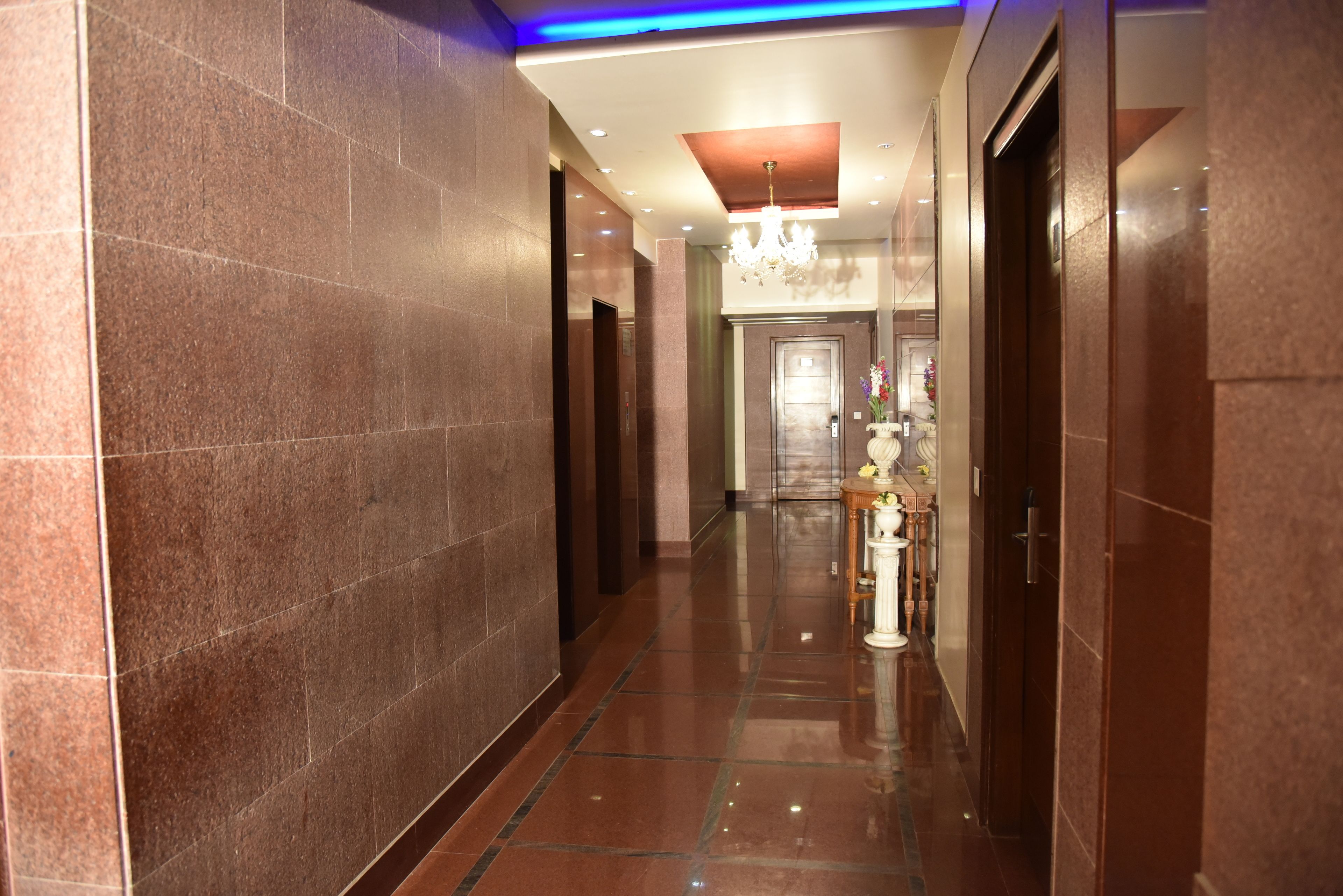 A corridor with marble walls, a chandelier, and a reception area with a vase of flowers.