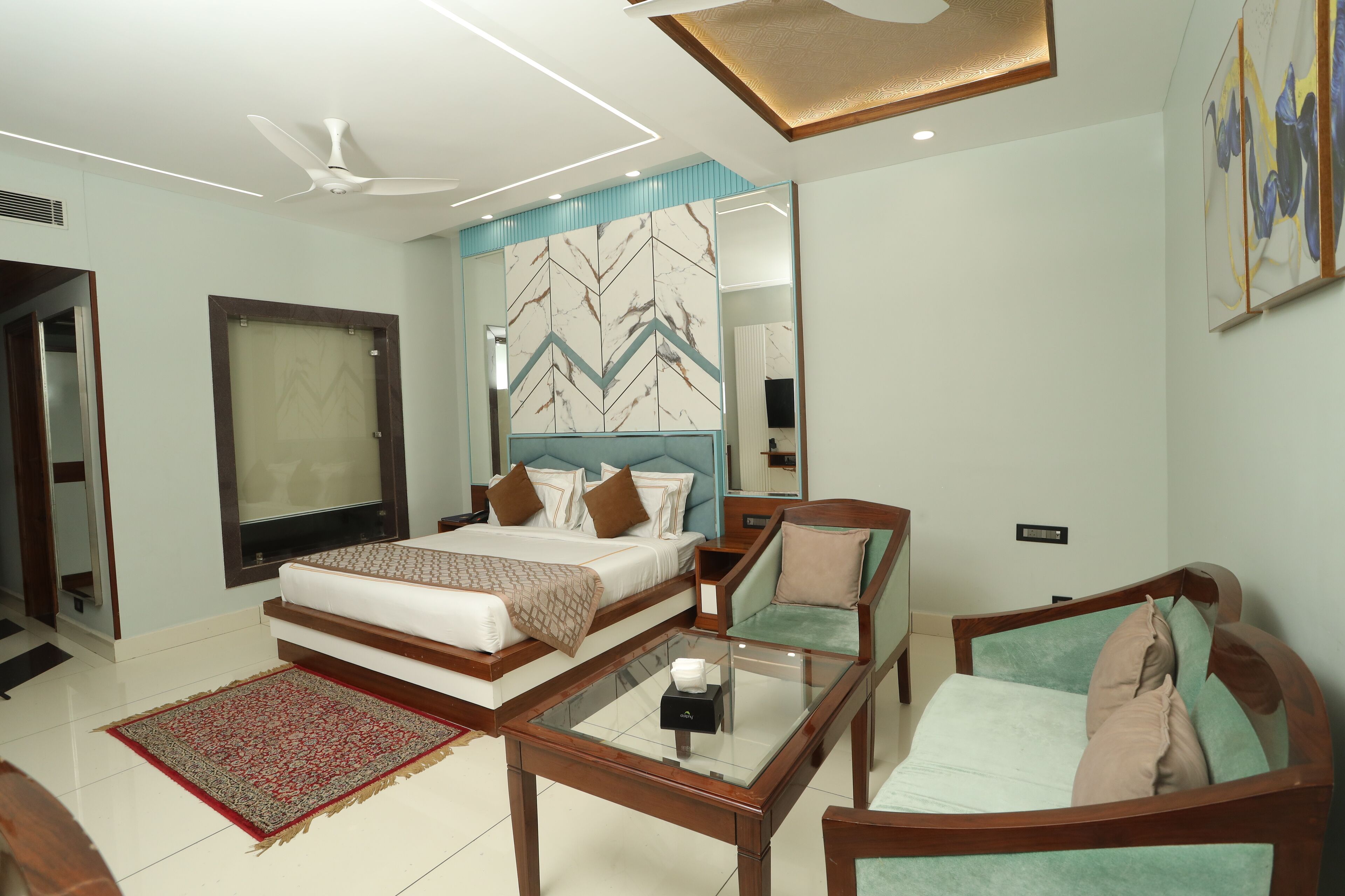 A hotel room with a bed, a sofa, a coffee table, a TV, and a ceiling fan.