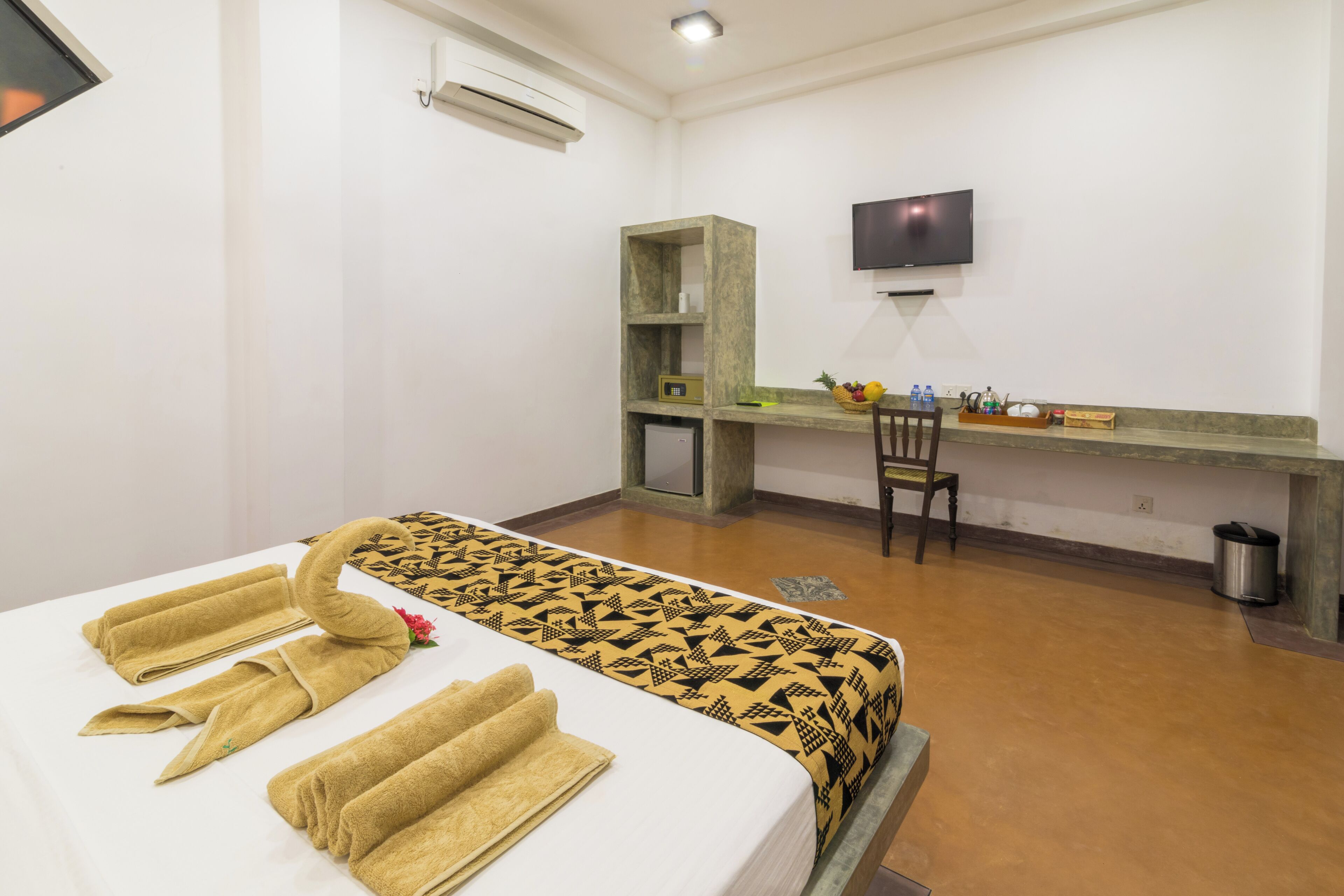 Una habitación de hotel con cama, escritorio, silla, televisor y cesto de basura.