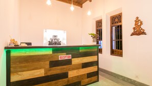 A reception desk with a 'RECEPTION' sign, wooden paneling, hanging pendant lights, and decorative wall art. - Green Villa (Unawatuna)