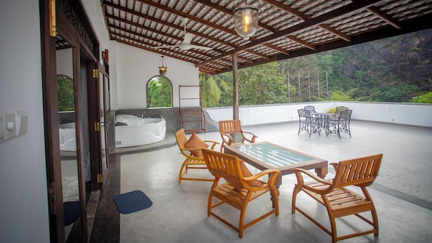 An outdoor patio with a wooden table and chairs, a glass-top table, and a view of a mountainous landscape. - Green Villa (Unawatuna)