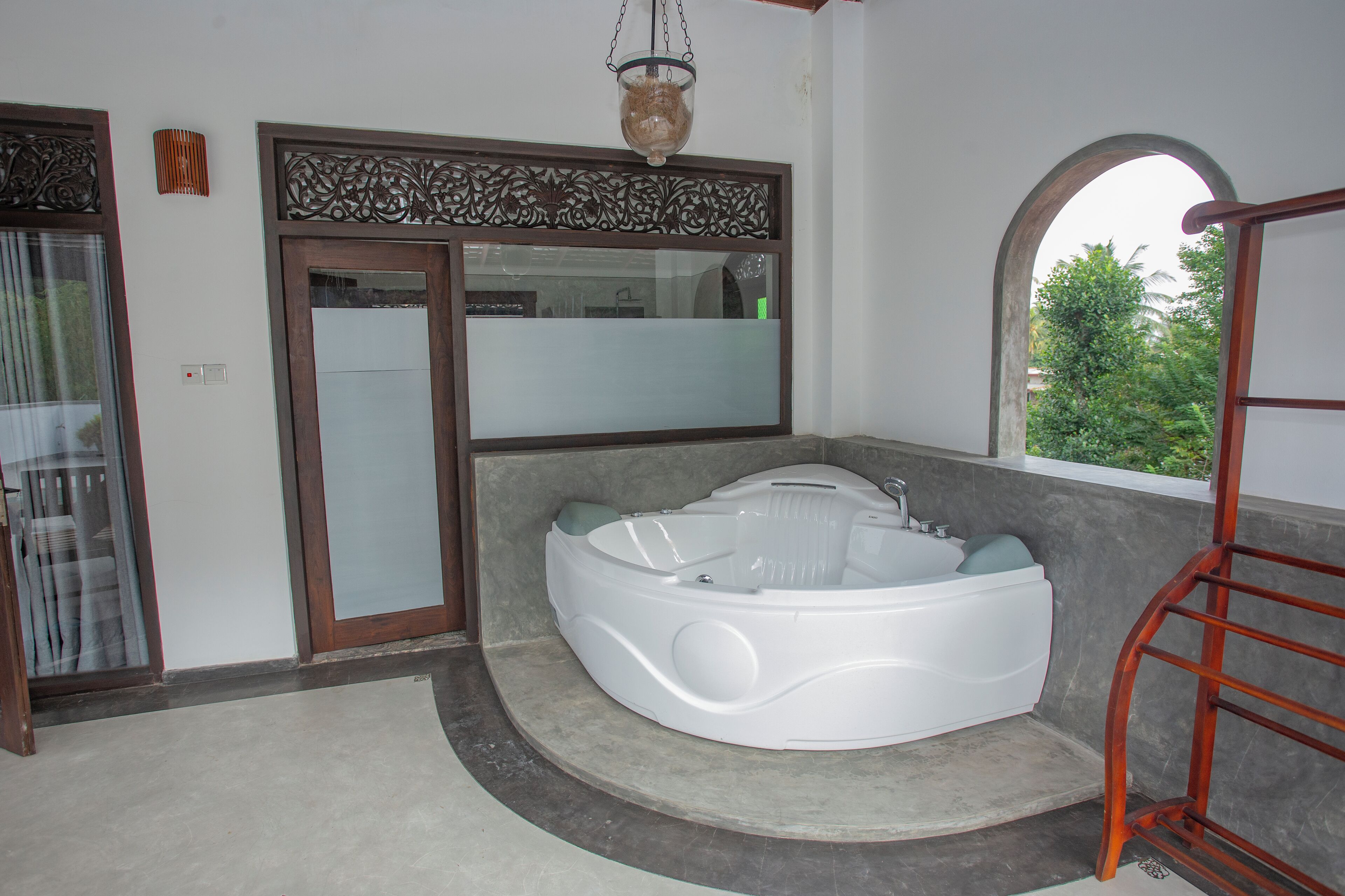 A modern bathroom with a large jacuzzi, a glass door, and a view of greenery outside.