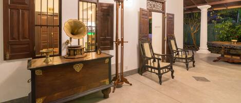 Una habitación con muebles de madera tradicionales, incluyendo un aparador con un tocadiscos, una lámpara de pie alta y dos sillas ornamentadas.