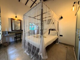 A bedroom with a four-poster bed, a bedside table, a chair, and a large mirror.