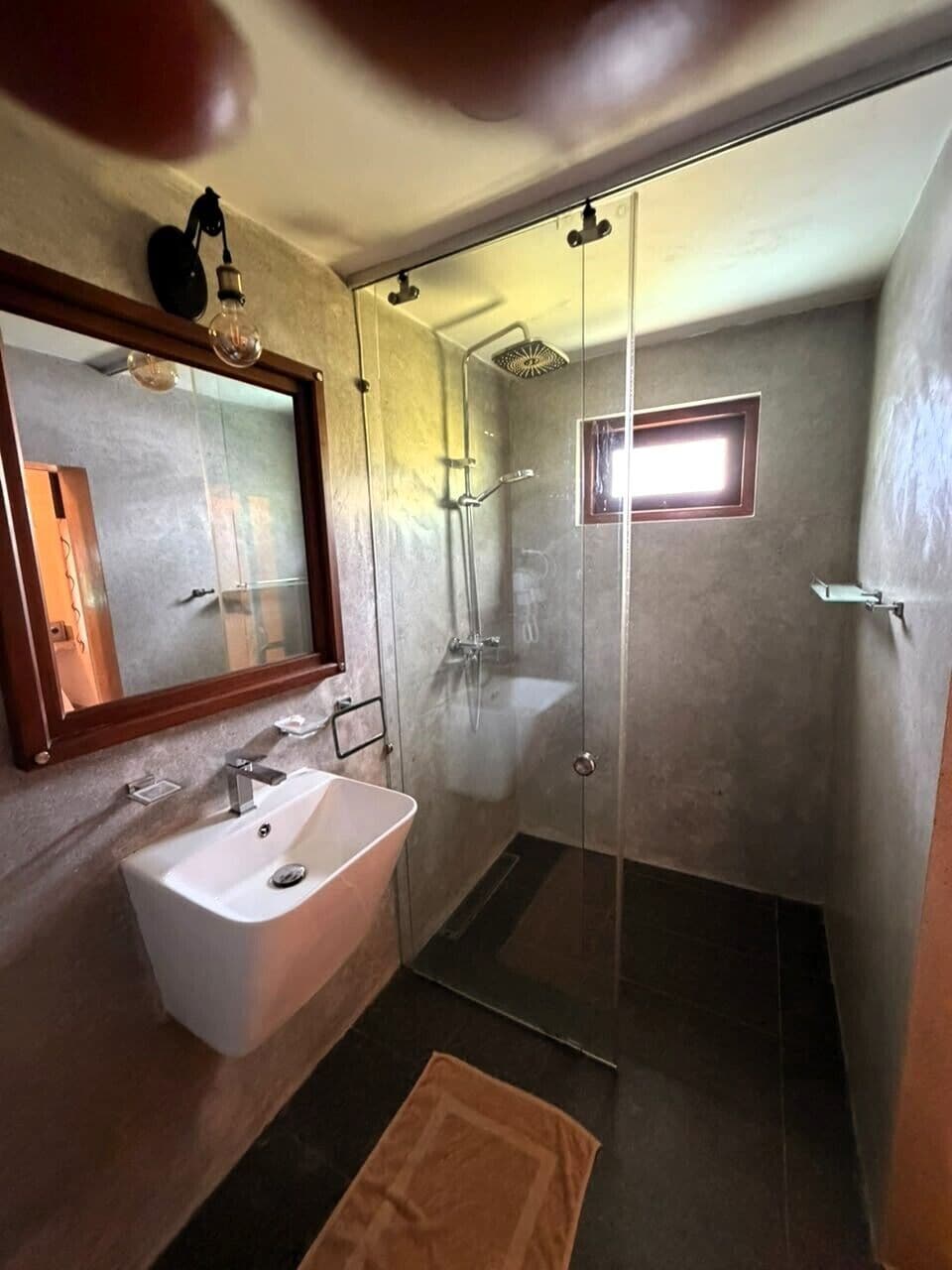 A bathroom with a white sink, a glass shower enclosure, and a mirror with a wooden frame.