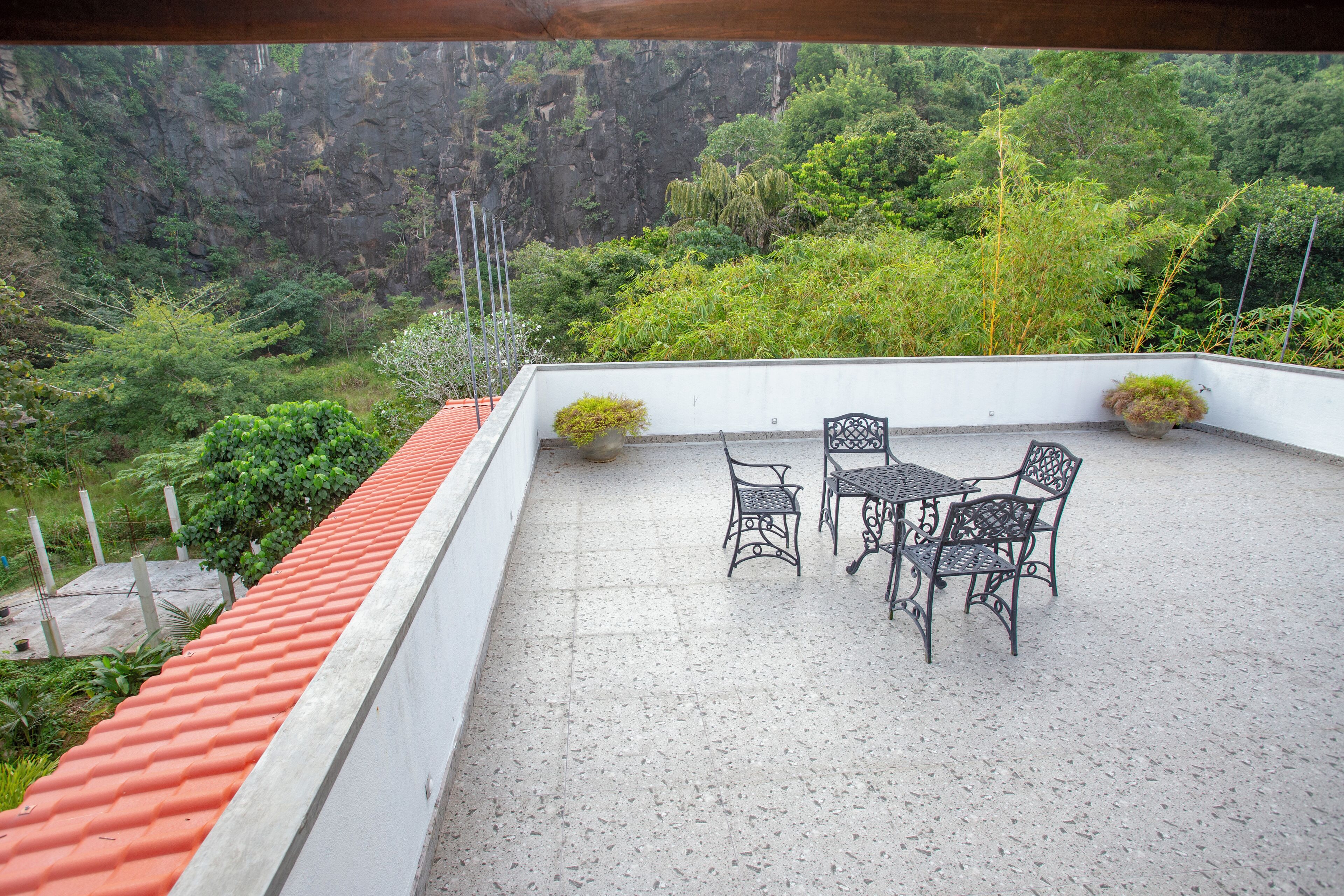 Una terraza con una mesa y sillas, rodeada de vegetación y un techo de tejas rojas.