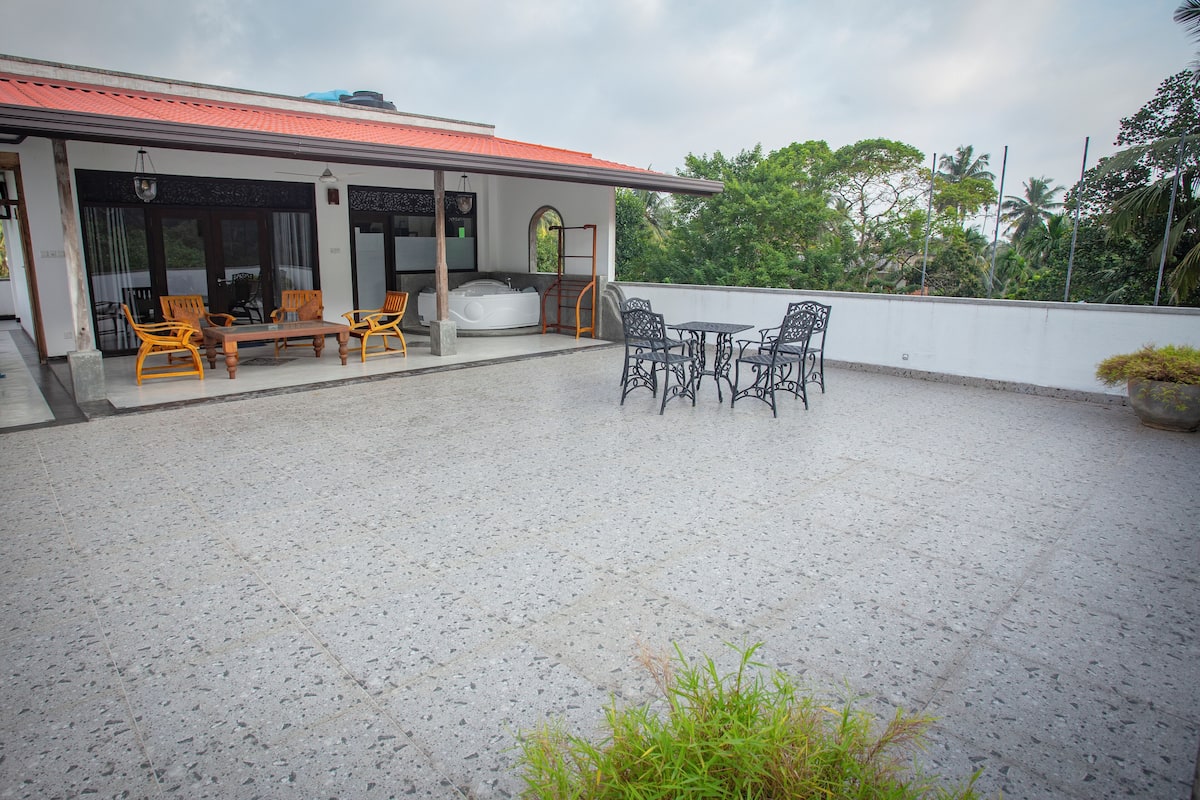A covered outdoor area with a seating arrangement, including a table and chairs, and a hot tub.