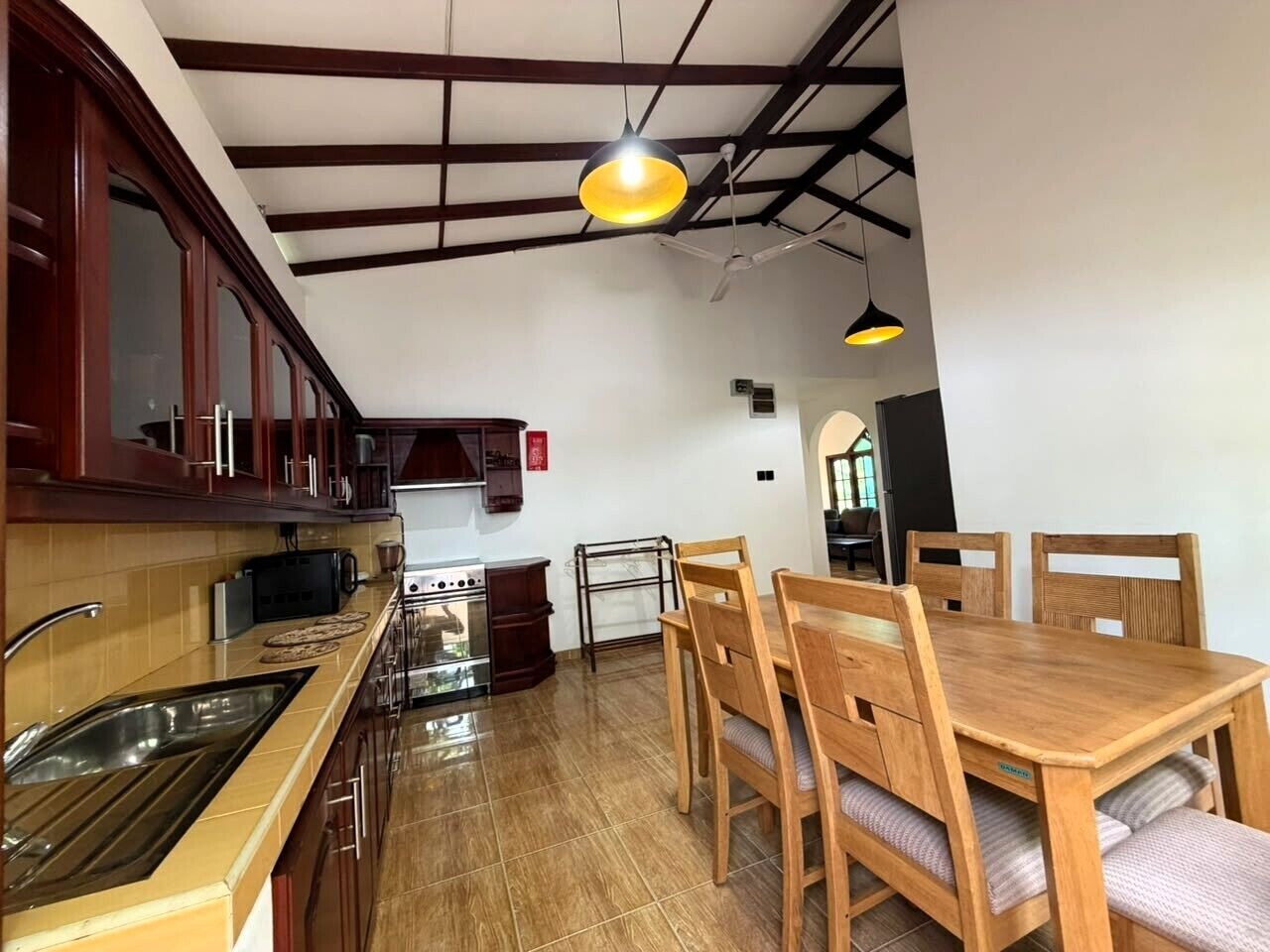 A kitchen with wooden cabinets, a dining table with chairs, a built-in oven, and a hanging pendant light.