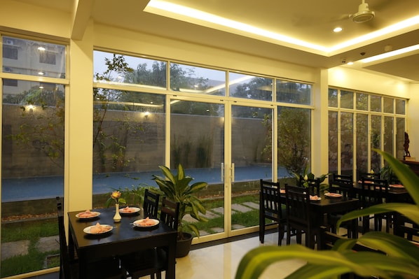 A dining area with large windows, a table set with plates, and potted plants.