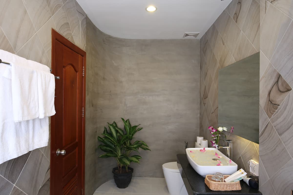 A bathroom with a wooden door, a potted plant, a sink with a mirror, and a toilet.