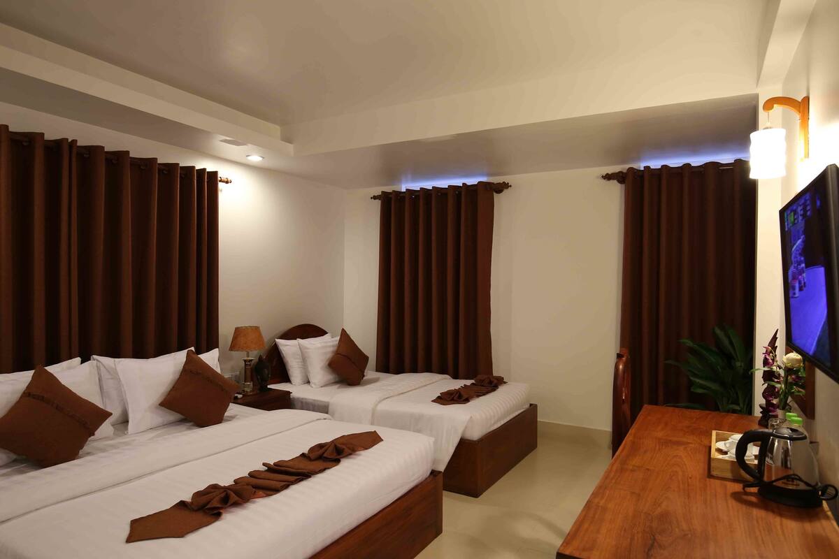 A hotel room with two beds, a wooden desk, a TV, and curtains.