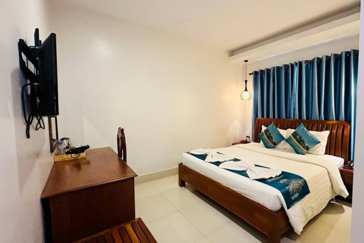 Una habitación de hotel con una cama, un escritorio, un televisor y un ventanal con cortinas.