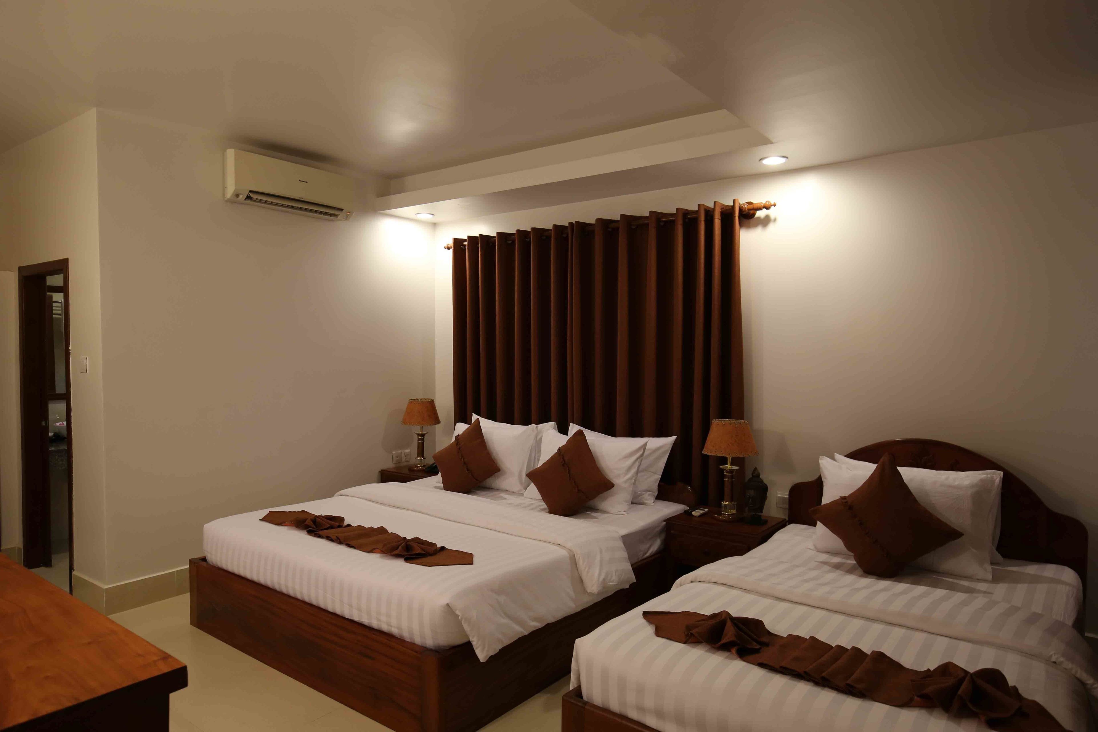 A hotel room with two beds, a wooden headboard, a nightstand with a lamp, and an air conditioning unit on the wall.