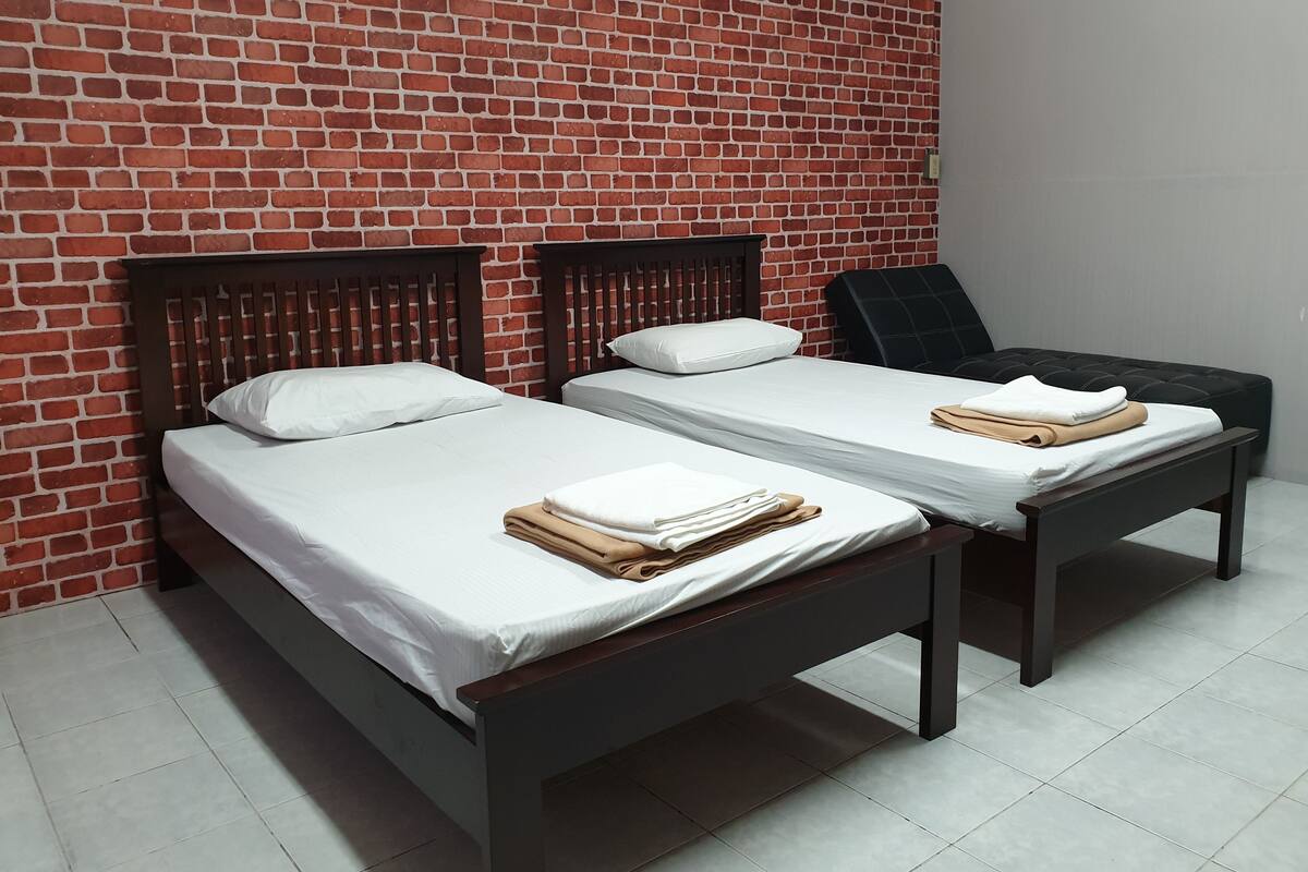 A room with two beds against a brick wall, each with a wooden headboard and white bedding.