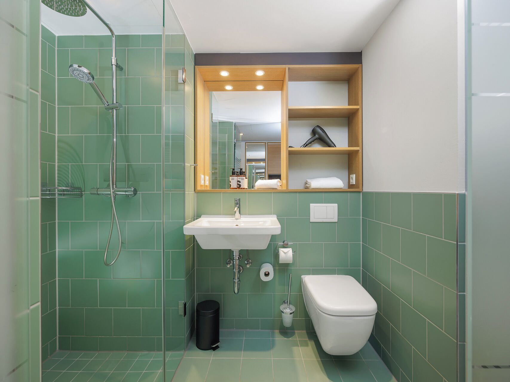 Un baño con ducha, lavamanos, inodoro y espejo con repisa superior.