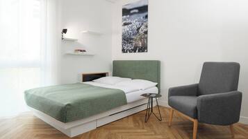 A modern bedroom with a bed, a chair, a bedside table, a wall-mounted shelf, and a picture.