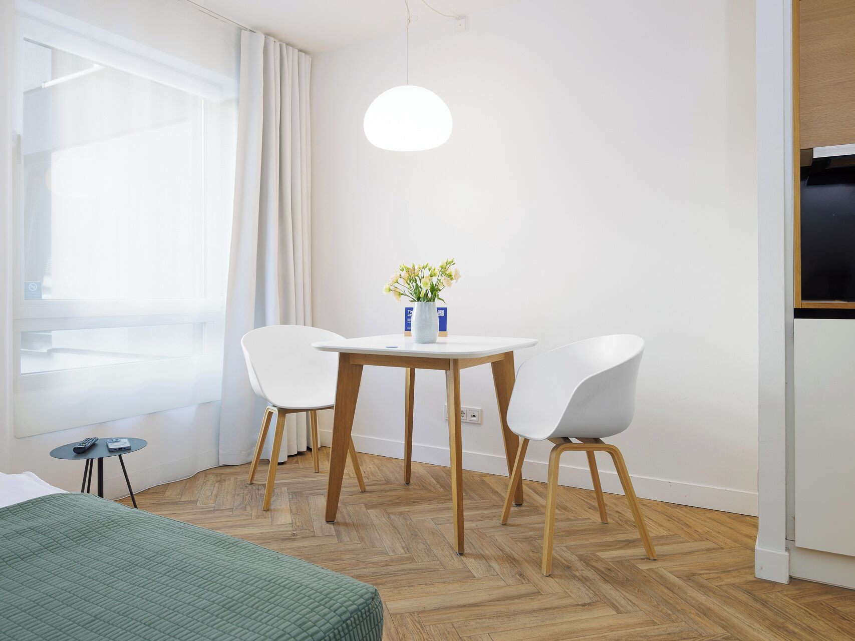 A modern room with a bed, a small table with chairs, a vase with flowers, and a television.