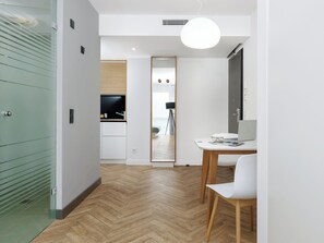 A modern interior with a herringbone floor, a dining area with a white table and chairs, and a kitchen with a built-in oven and sink. - smartments München Parkstadt Schwabing (Munich)