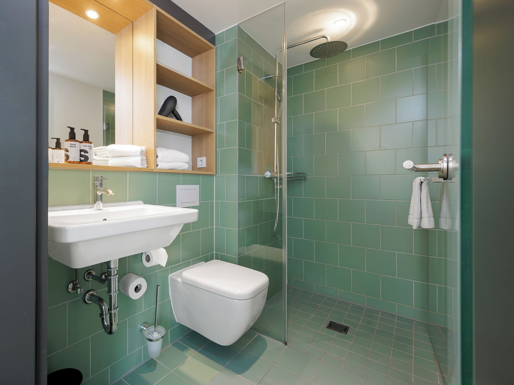 A modern bathroom with a shower, toilet, sink, and a shelf with toiletries.