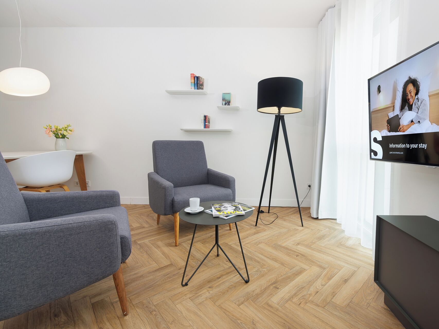 Un salon moderne avec un canapé gris, une table basse sur laquelle sont posés des magazines, un lampadaire et un téléviseur qui affiche un message de bienvenue.