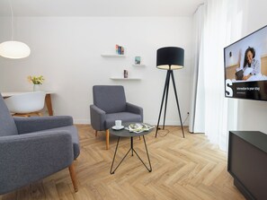 Un salon moderne avec un canapé gris, une table basse sur laquelle sont posés des magazines, un lampadaire et un téléviseur qui affiche un message de bienvenue.
