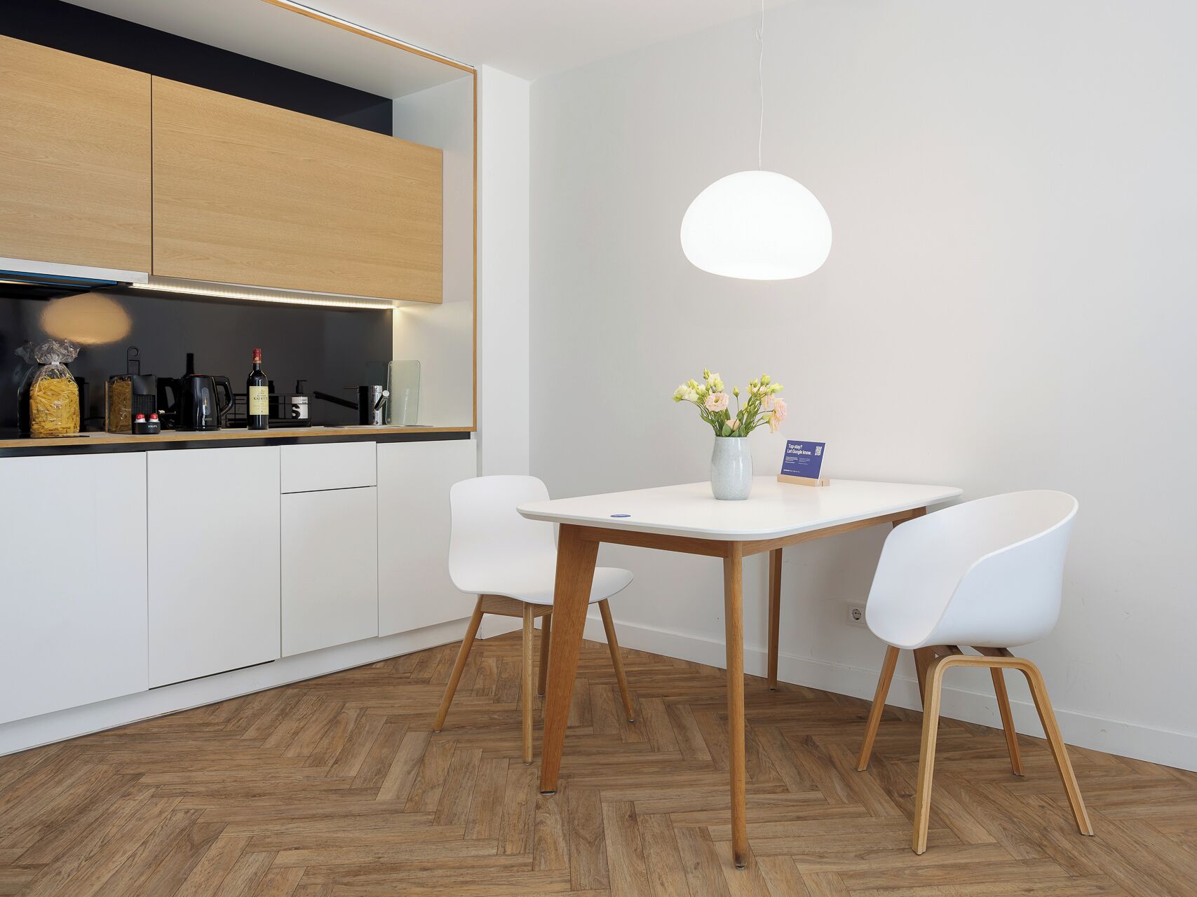 A modern kitchen with white cabinets, a wooden herringbone floor, and a dining area with a white table and chairs.