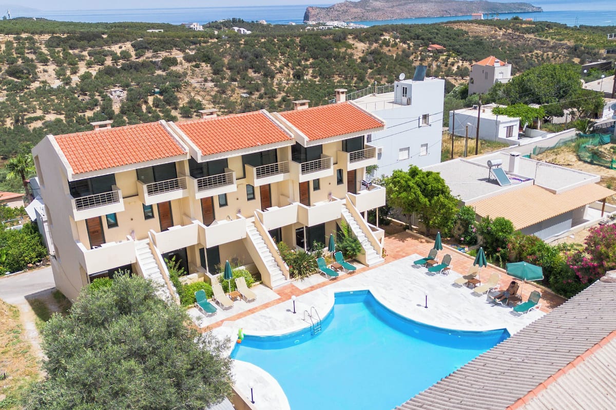 A multi-story hotel with a swimming pool, outdoor seating, and a view of the sea.