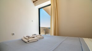 A neatly made bed with a grey textured bedspread and a stack of folded towels on the side. - Orestis Hotel Apartments (Chania)