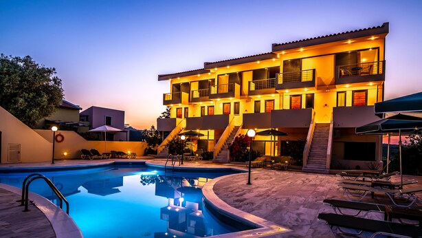 A modern building with a swimming pool, outdoor seating, and a staircase leading to the upper floors. - Orestis Hotel Apartments (Chania)