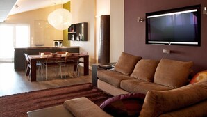 Ett modernt vardagsrum med en stor platt-TV som är monterad på väggen, en brun lädersoffa och en matplats med ett glasbord och stolar.