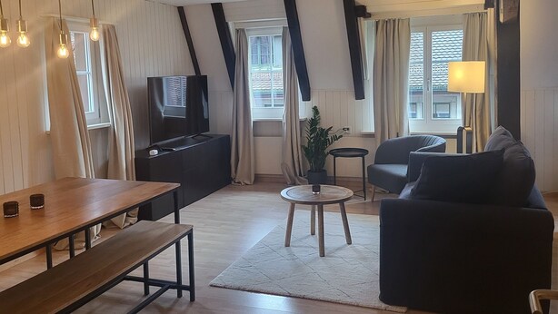 Una sala moderna con una mesa de comedor de madera, un sofá, un televisor y una lámpara.