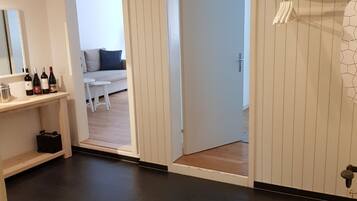 A room with a dark floor, a white door, a white wall with a shelf, and a white ceiling.