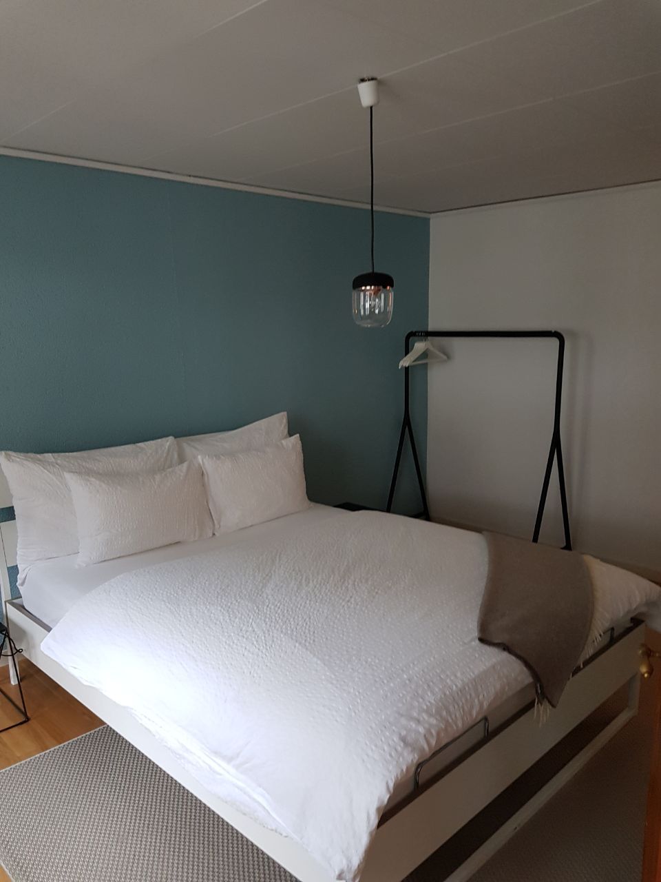 A single-bed room with a white bed, a hanging light fixture, and a wall-mounted hanger.