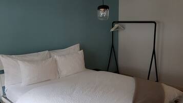 A single-bed room with a white bed, a hanging light fixture, and a wall-mounted hanger.