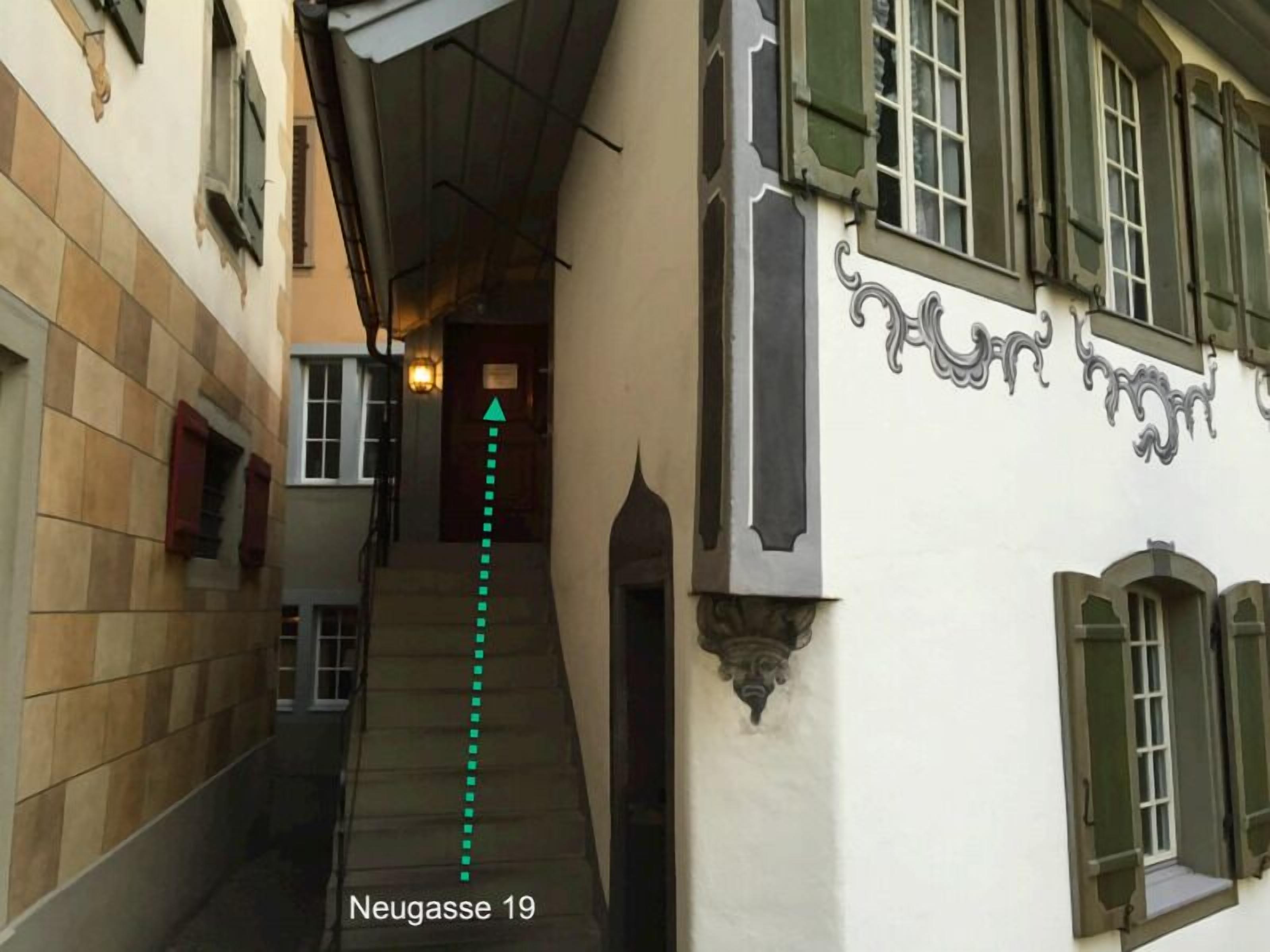 A narrow alleyway with a staircase leading to a door marked "Neugasse 19".