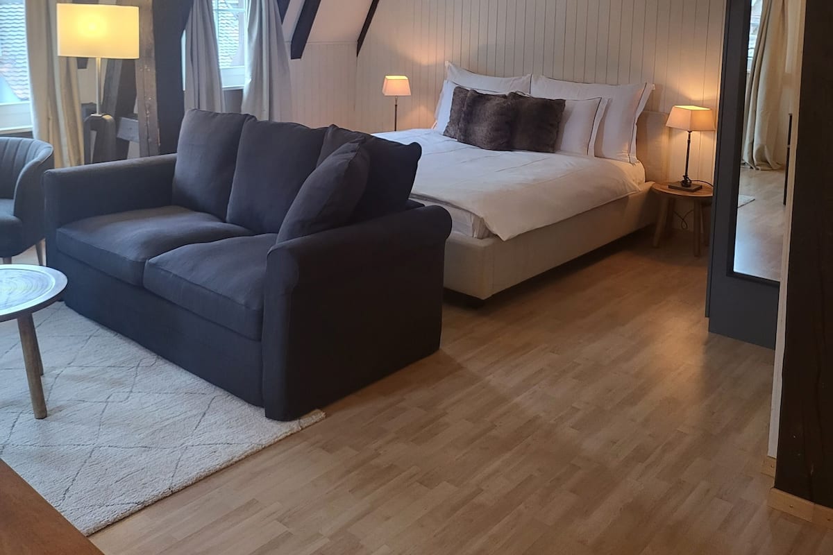 A modern bedroom with a bed, a sofa, and two bedside tables with lamps.