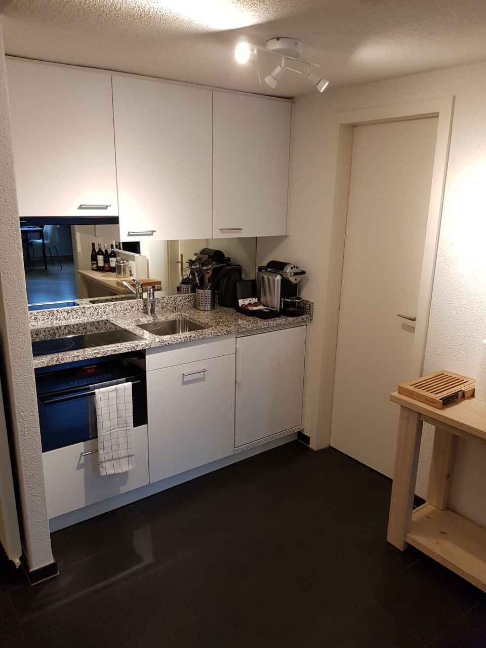 Una cocina compacta con armarios blancos, encimera de granito, horno integrado y cafetera.