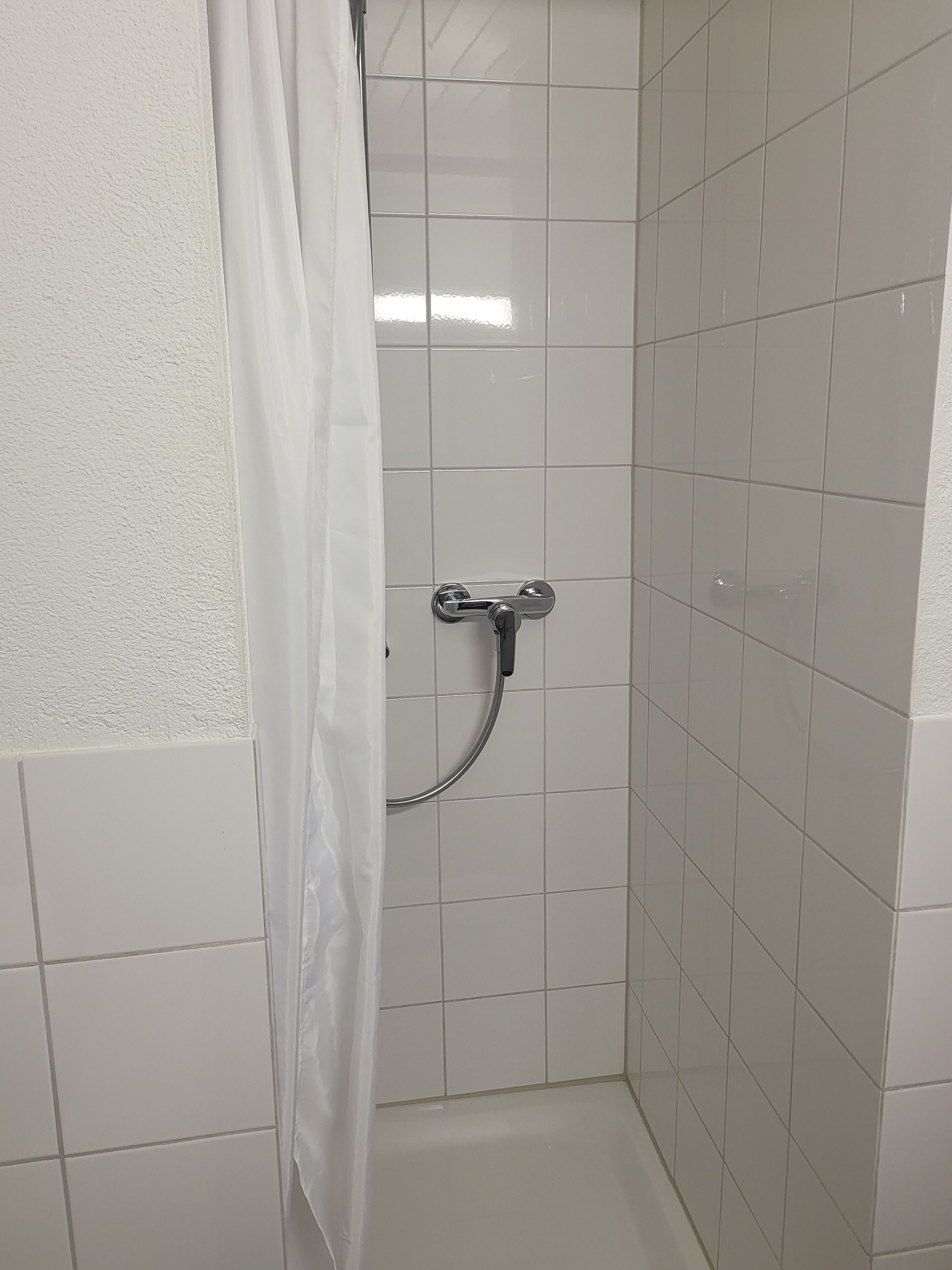 A small, tiled shower room with a showerhead and a curtain.