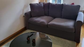 A living room with a sofa, a round coffee table, a lamp, and a window with curtains.