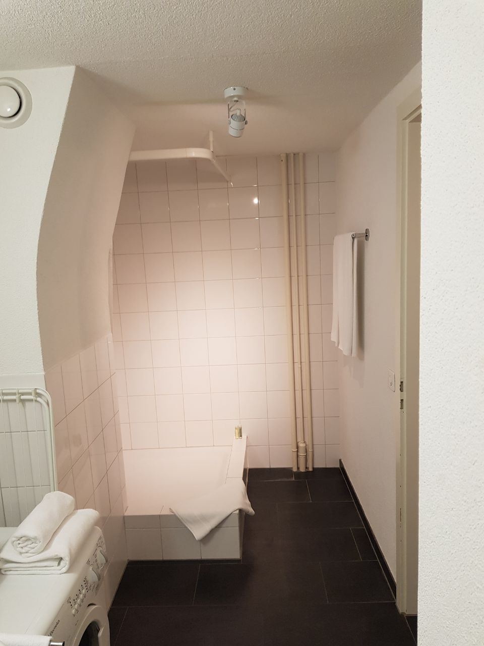 A compact bathroom with a white tiled shower, a small sink with a towel, and a toilet.