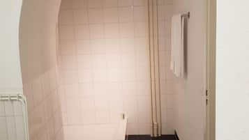 A compact bathroom with a white tiled shower, a small sink with a towel, and a toilet.